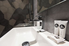 A modern bathroom with a white sink, a glass shower enclosure, and a hexagonal tile backsplash. - Five Boutique Rooms (Naples)