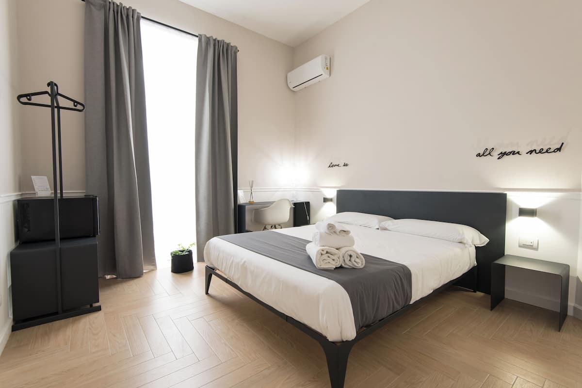 A modern hotel room with a neatly made bed, a side table, a desk, and a coat rack.
