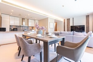 Ein modernes Wohnzimmer mit Essbereich, einer Couch, einem Fernseher und einer Küche im Hintergrund.