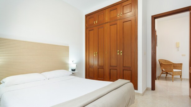 Une chambre à coucher avec un grand lit, une armoire en bois et un fauteuil en osier.