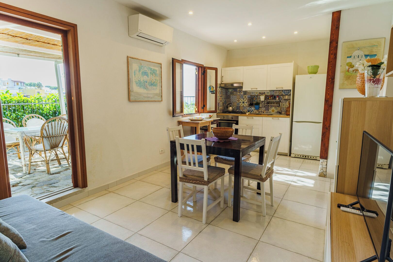 A dining area with a table and chairs, a kitchen with cabinets and appliances, and a view through a glass door to an outdoor patio.