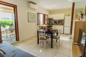 A dining area with a table and chairs, a kitchen with cabinets and appliances, and a view through a glass door to an outdoor patio. - Complesso Villa Le Palme (Forio)