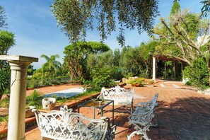 A garden patio with white wrought iron furniture, a stone column, and a pergola. - Complesso Villa Le Palme (Forio)