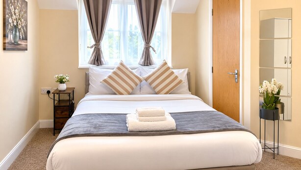 A neatly arranged bedroom with a bed, pillows, a bedside table with a vase, and a door. - Modern 2BR House Sleeps 6 Parking, Wi-Fi & Self Check-In Near Bluewater & London (Greenhithe)