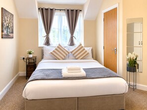 A neatly arranged bedroom with a bed, pillows, a bedside table with a vase, and a door. - Modern 2BR House Sleeps 6 Parking, Wi-Fi & Self Check-In Near Bluewater & London (Greenhithe)