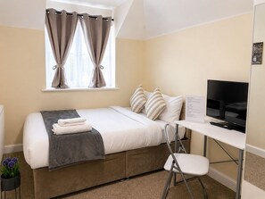 A bedroom with a bed, a desk, a chair, a television, and a window with curtains. - Modern 2BR House Sleeps 6 Parking, Wi-Fi & Self Check-In Near Bluewater & London (Greenhithe)