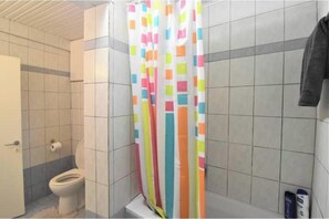 Un baño con cortina de ducha, inodoro y paredes de azulejos.