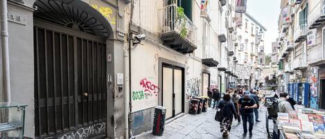 A narrow street with buildings, a closed shop with graffiti, and a street vendor with books.