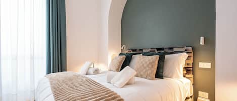 A modern bedroom with a large bed, a headboard with a geometric pattern, a bedside table, and a wall-mounted light fixture.