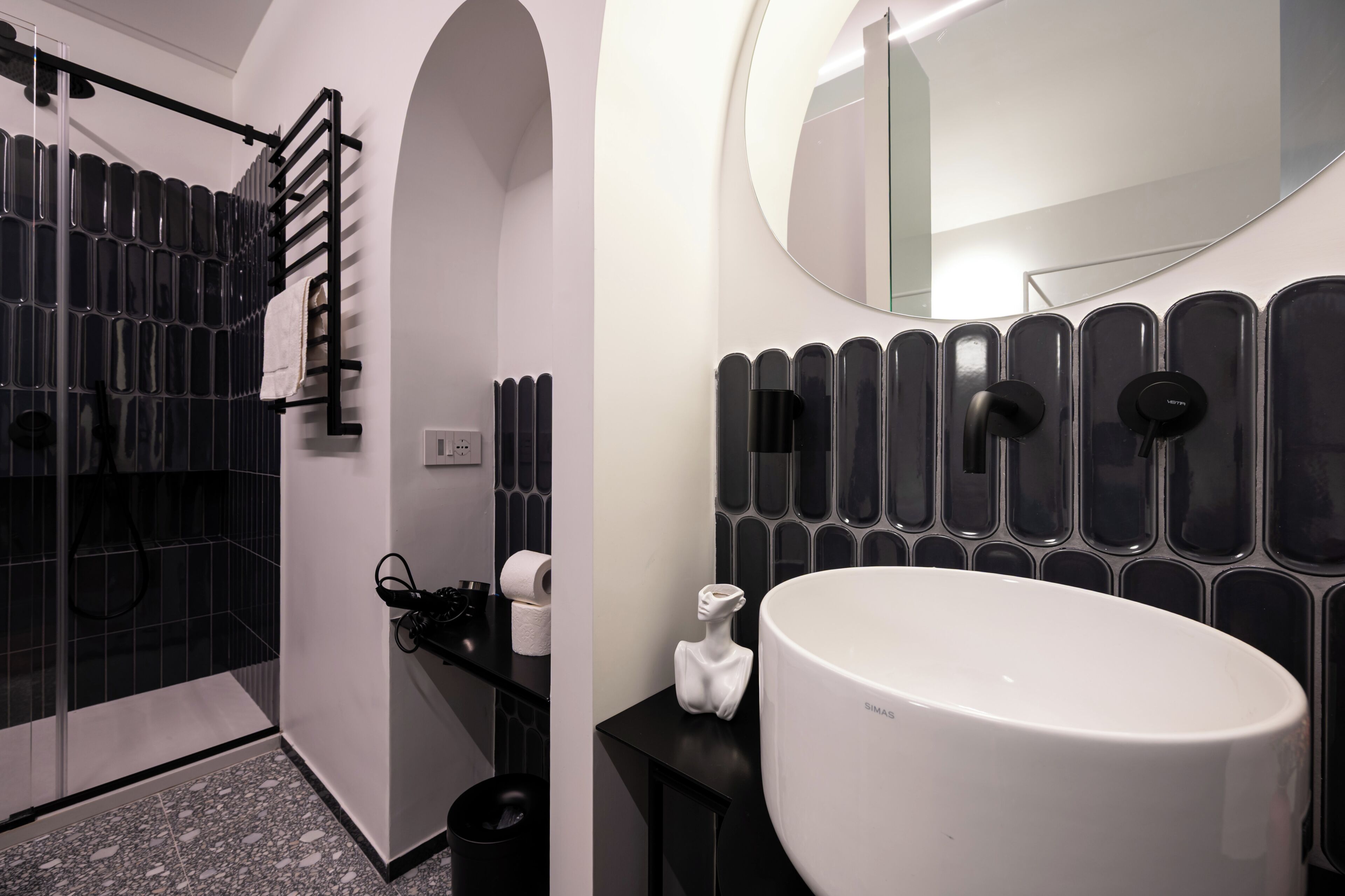 A modern bathroom with a large white sink, black towel rack, and a shower area with a glass door.
