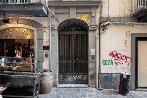Un edificio con una puerta metálica cerrada, grafitis en la pared y un bote de basura en la acera.