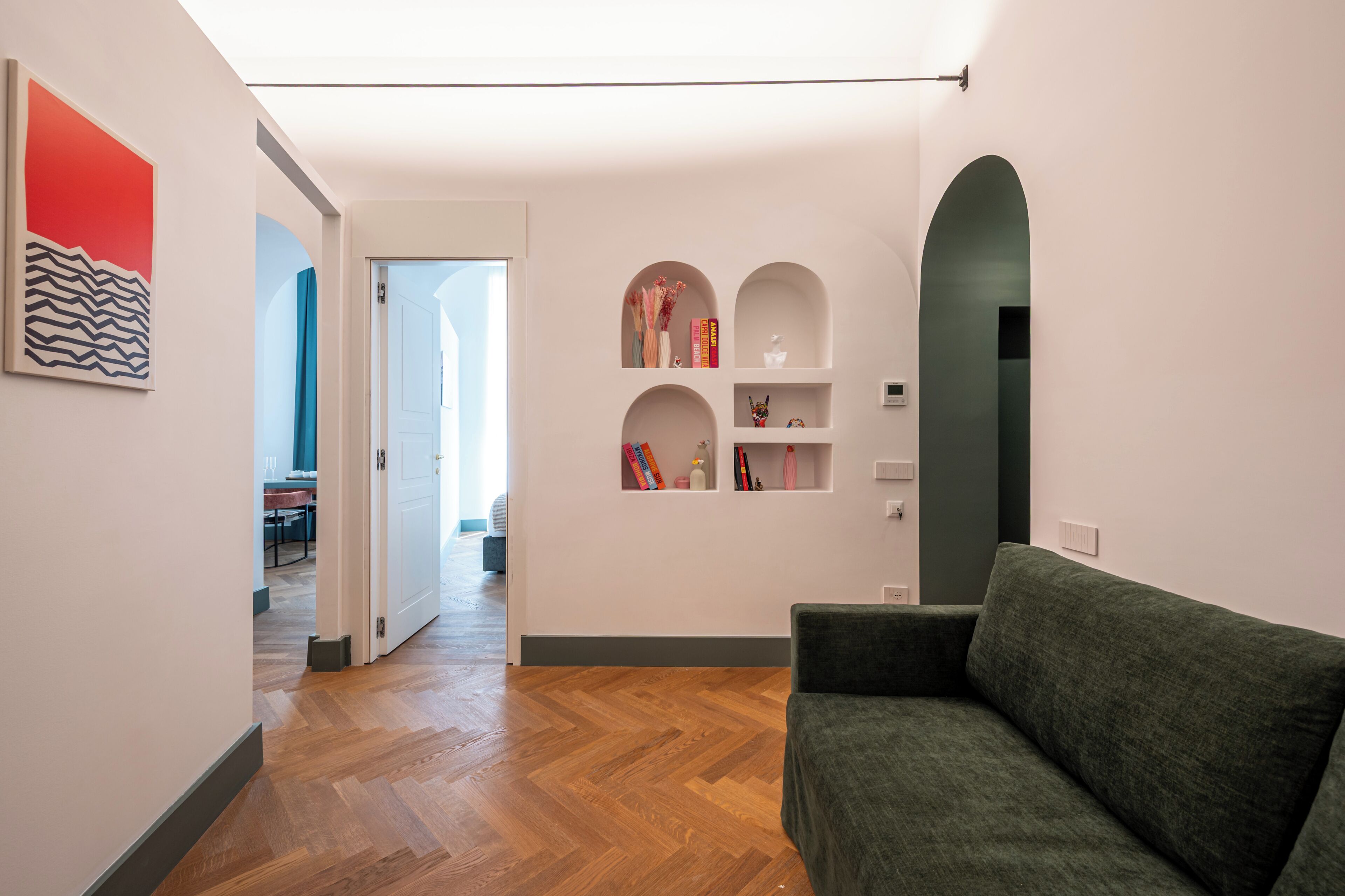 A modern interior with a wooden floor, a green sofa, and a hallway leading to another room.
