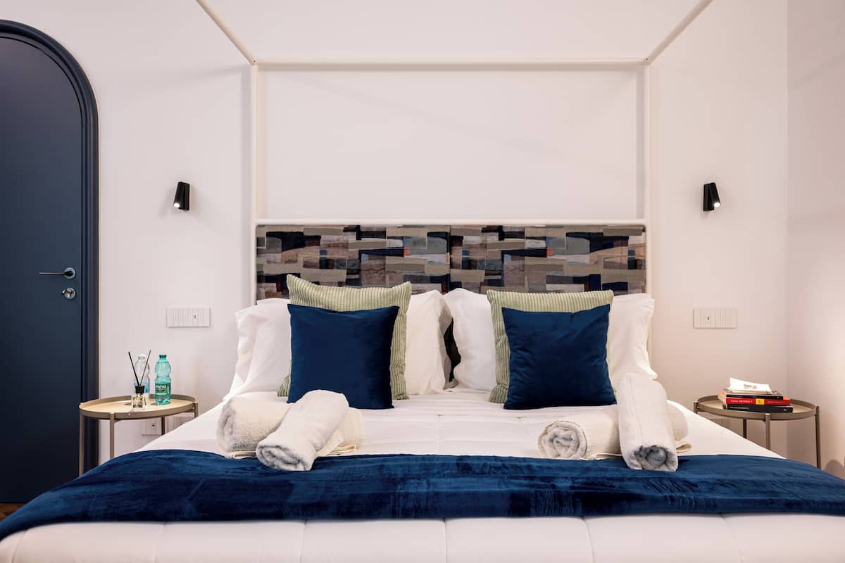 A modern hotel room with a large bed, two bedside tables, a headboard with a geometric pattern, and a door.
