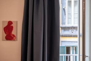 A room with a view of a building through a window, a red artwork on the wall, and a curtain partially drawn. - Via Port'Alba 19 (Naples)