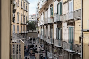 A narrow street with multi-story buildings, balconies, and a visible bridge. - Via Port'Alba 19 (Naples)