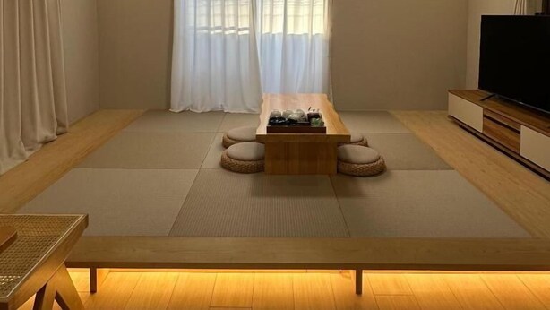 A minimalist living room with tatami mats, a low wooden table, a flat-screen TV, and an air conditioning unit. - Dc Sakura Hotel-HitomiHouse (Osaka)