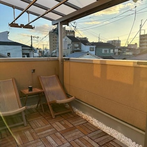 A balcony with wooden flooring, two wicker chairs, and a small table. - Dc Sakura Hotel-HitomiHouse (Osaka)