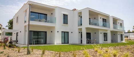 Um edifício residencial moderno de dois andares com varandas, janelas amplas e um gramado bem cuidado.