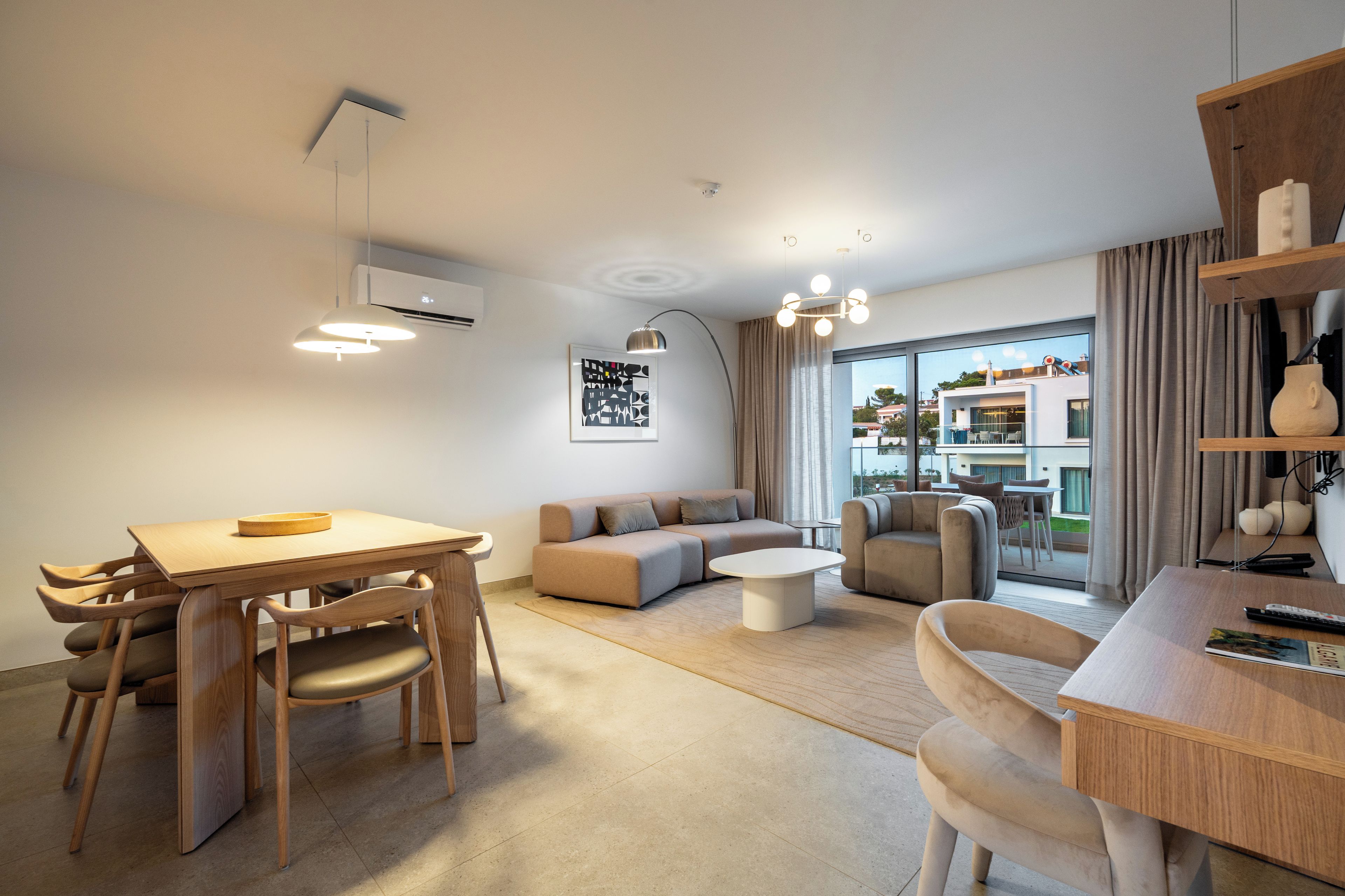 A modern living room with a dining area, sofas, and a large window offering a view of the outside.