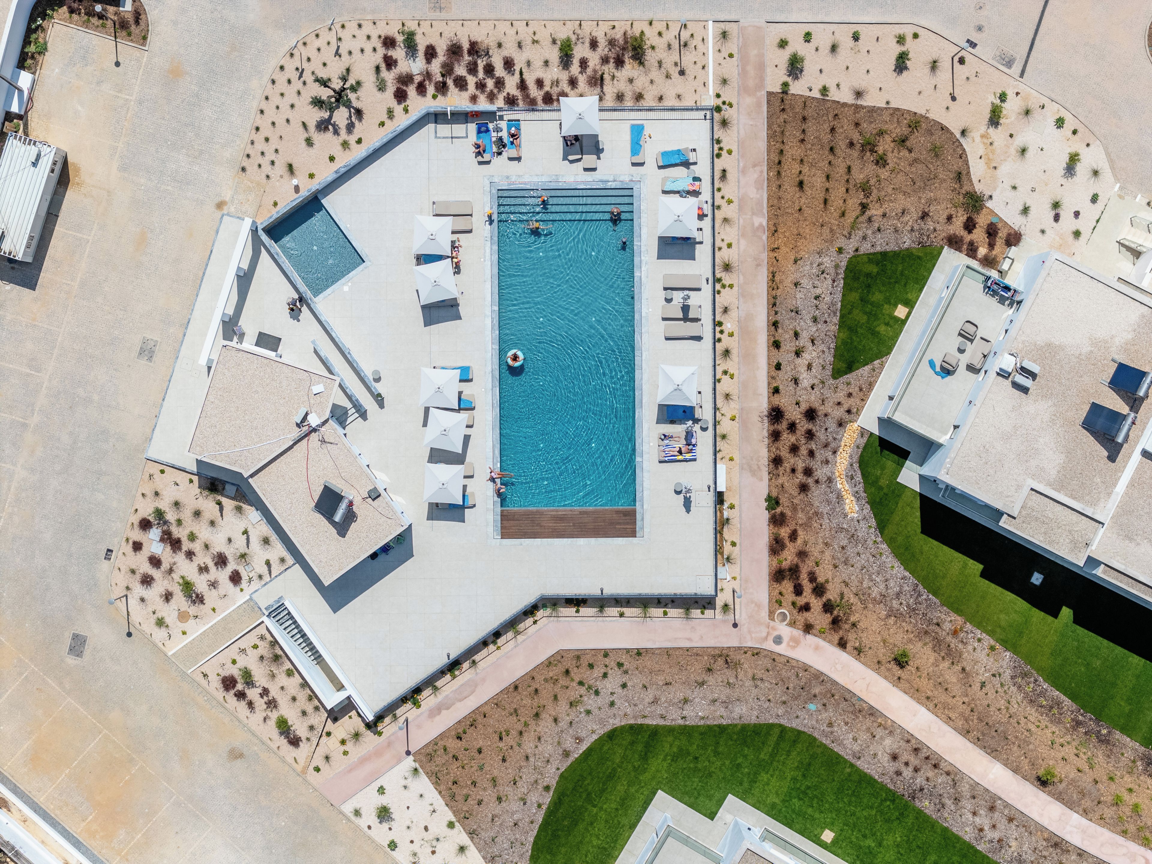 Vue aérienne d’un complexe hôtelier doté d’une piscine, de chaises longues et d’un jardin aménagé.