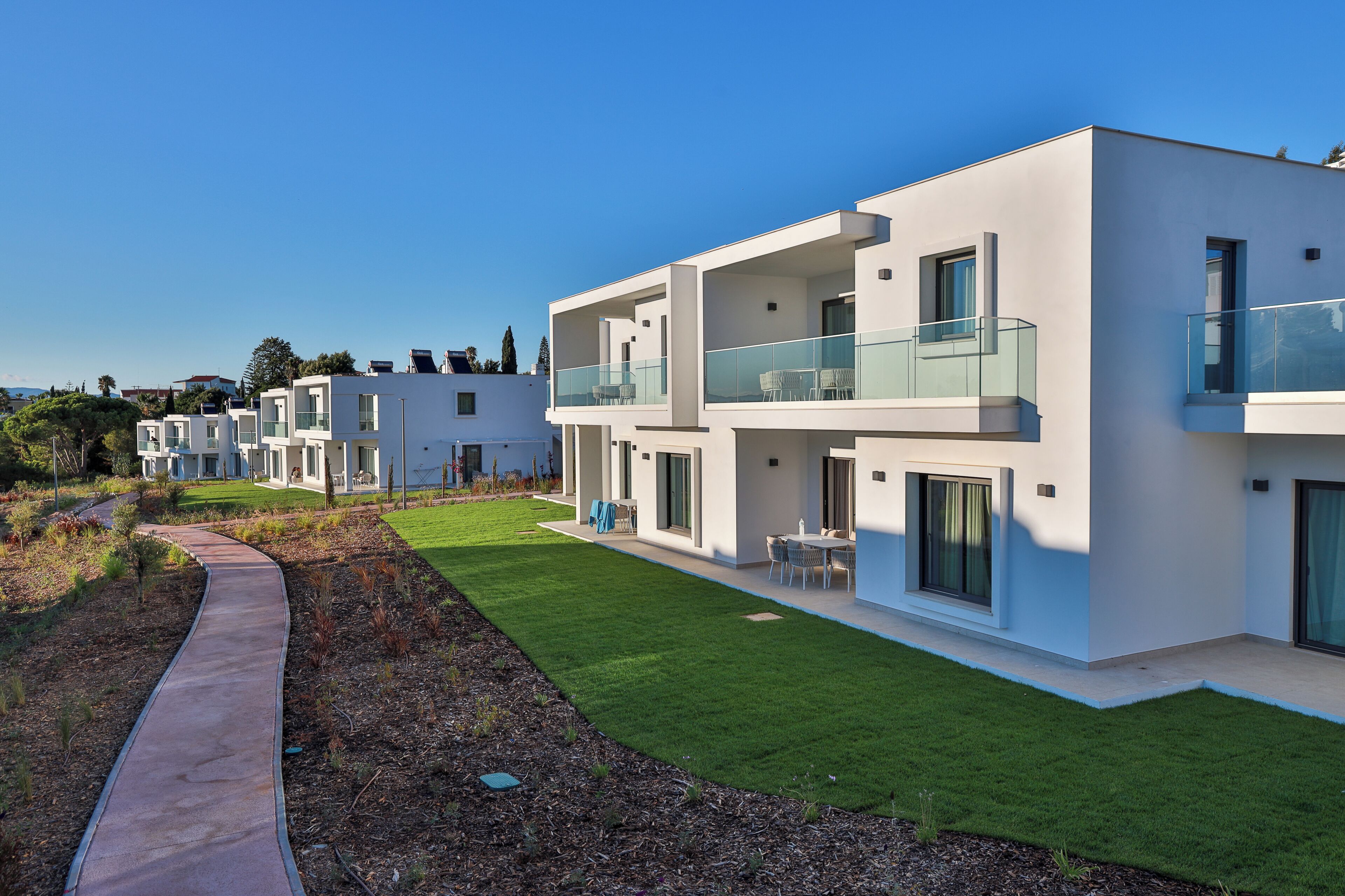 A modern multi-story residential building with balconies, a well-maintained lawn, and a clear sky.