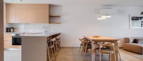 A modern kitchen with wooden cabinets, a built-in oven, and a dining area with a table and chairs.