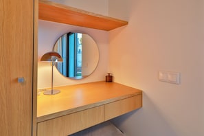 Une coiffeuse en bois, ornée d’un miroir rond, d’une lampe et d’un petit flacon posé sur le plateau.