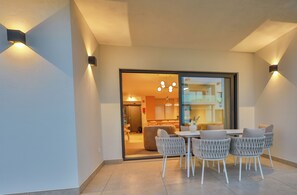 An outdoor seating area with a table and chairs, a sliding glass door leading to a kitchen, and wall-mounted lights. - Primelife Carvoeiro (Carvoeiro)