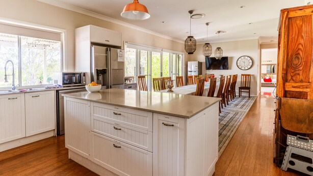 Een moderne keuken met witte kastjes, een groot eiland en een eethoek met houten stoelen.