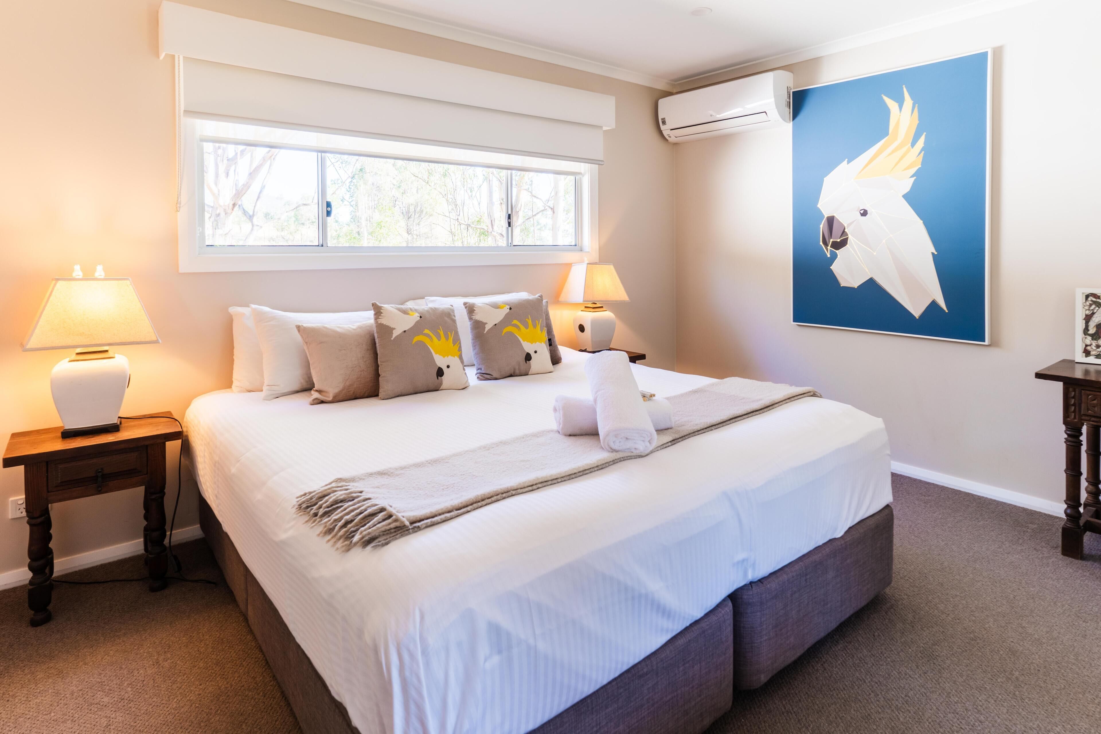A neatly made bed with pillows, a bedside lamp, and a wall-mounted air conditioner.