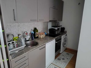 Eine kompakte Küche mit Spüle, Waschmaschine und einer Arbeitsfläche mit verschiedenen Gegenständen.
