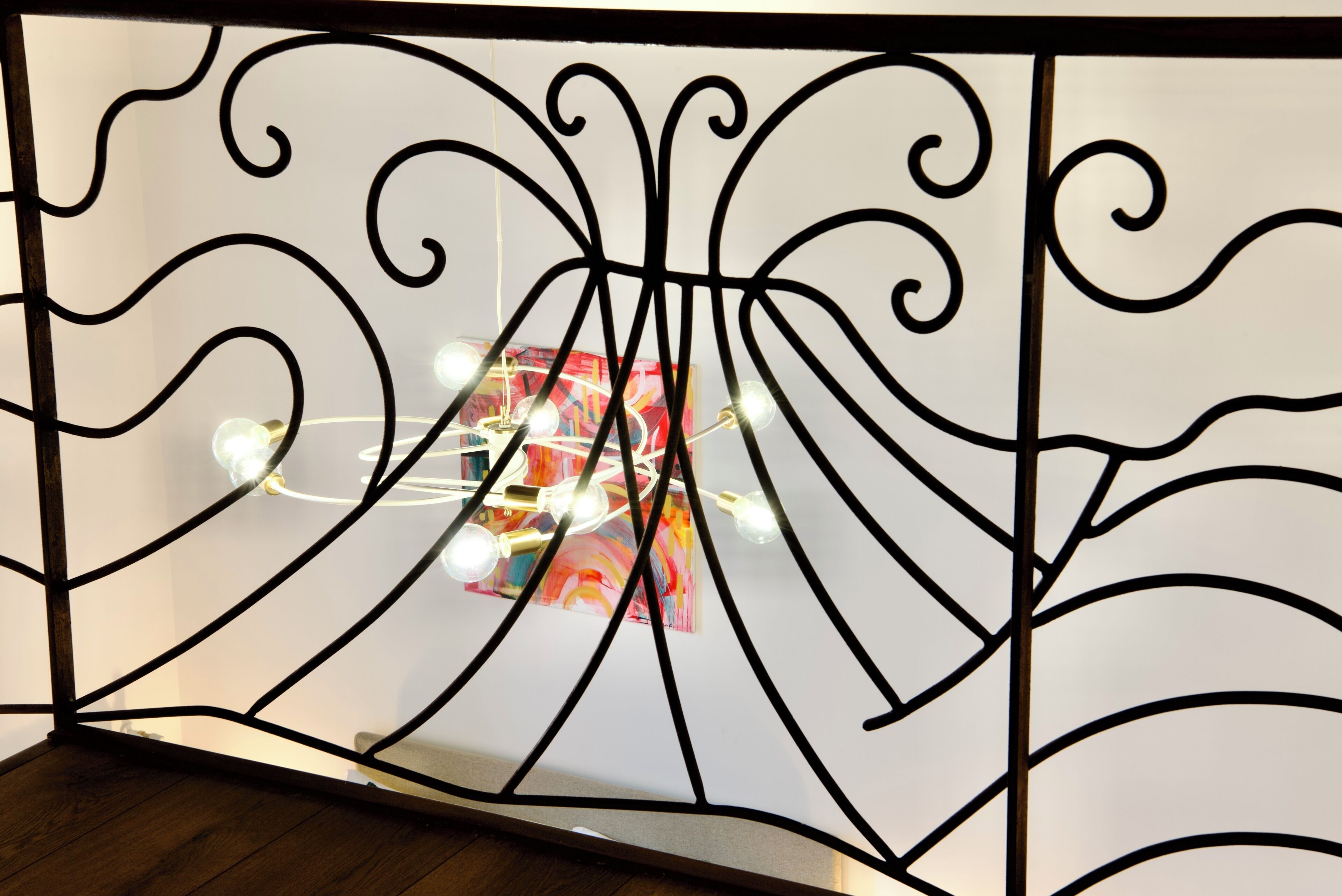 A room with a white wall, a black metal partition with a geometric design, and a light fixture with multiple bulbs.