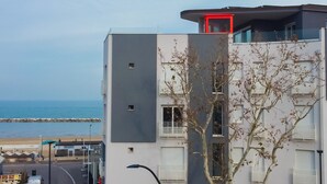 Een meerhoog gebouw met balkon, uitzicht op zee en een boom ervoor.
