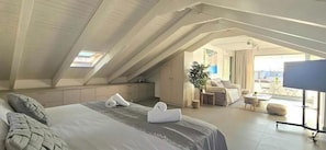A hotel room with a bed, a seating area with a table and chairs, a TV, and a balcony with a view. - Kyvetos Loft Apartment (Zakinthos)
