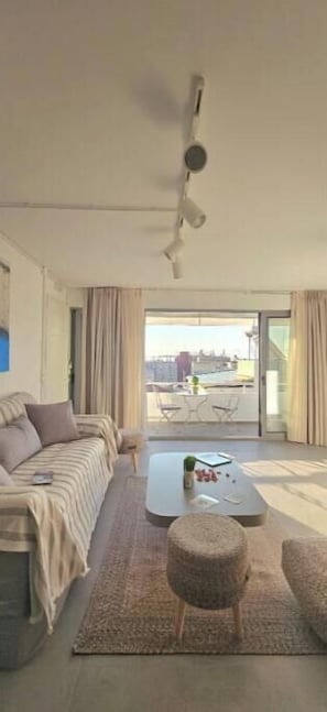 A modern living room with a sofa, coffee table, and ottoman, a ceiling fan, and a view to an outdoor balcony area. - Kyvetos Loft Apartment (Zakinthos)