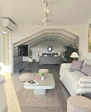 A modern loft bedroom with a sloped ceiling, a bed with a circular window, a sofa, a coffee table, and a floor lamp. - Kyvetos Loft Apartment (Zakinthos)