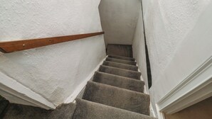 A narrow stairway with a wooden handrail, carpeted steps, and white walls. - The Cottage (Budleigh Salterton)