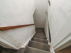 Una escalera estrecha con barandilla de madera, escalones alfombrados y paredes blancas.