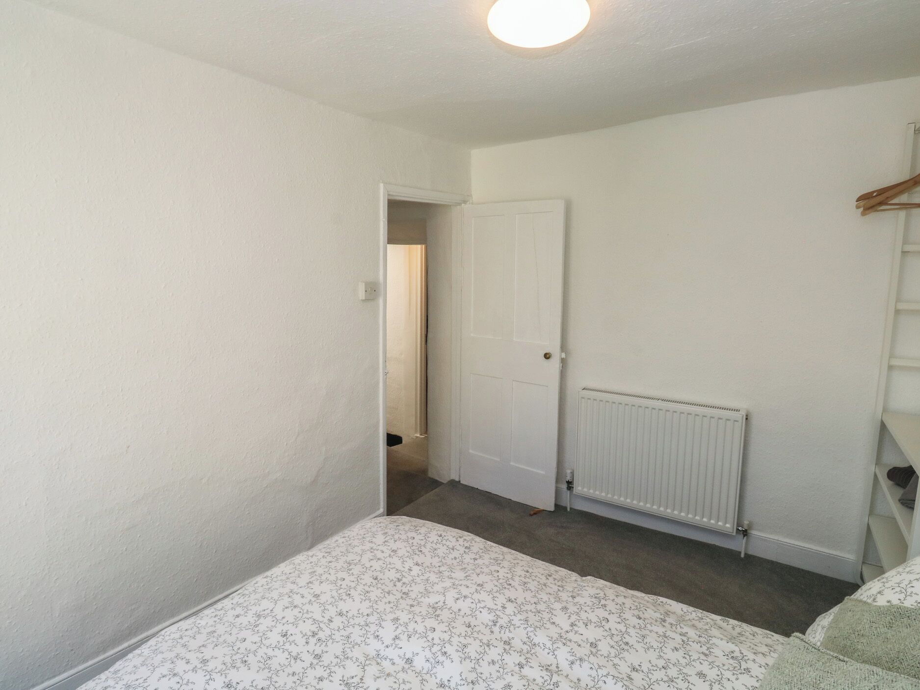 Une chambre à coucher avec un lit, un radiateur, une porte et un couloir menant à une autre pièce.