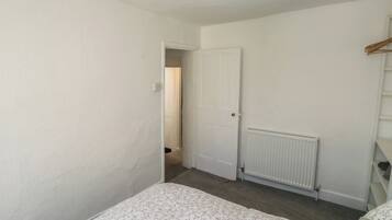 Une chambre à coucher avec un lit, un radiateur, une porte et un couloir menant à une autre pièce.
