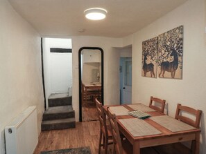 A dining area with a wooden table and chairs, a staircase, and a hallway leading to another room. - The Cottage (Budleigh Salterton)