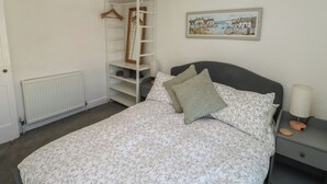 A bedroom with a bed, a nightstand, a dresser, a radiator, a wardrobe, and a framed picture on the wall.