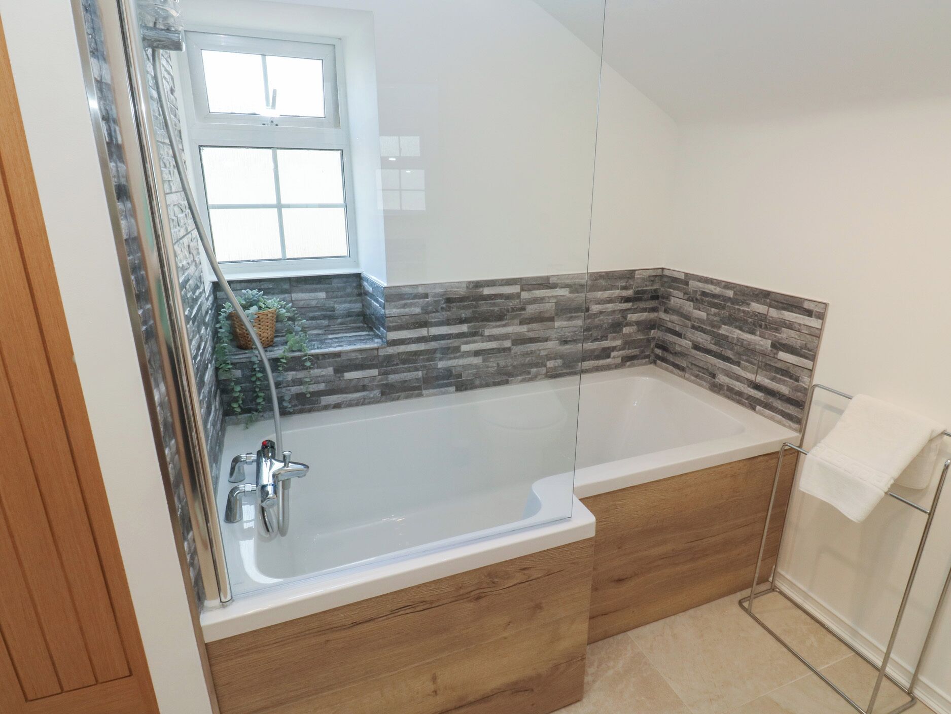 Une salle de bain moderne avec une baignoire sur pieds, un meuble-lavabo en bois et un pare-feu en pierre.