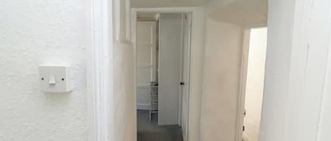 A narrow hallway with white walls, a white door at the end, and a light switch on the left.