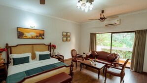 A hotel room with a bed, a sofa, a bench, a coffee table, a ceiling fan, an air conditioner, and a window with a view. - Reebah Inn & Suites (Vagator)