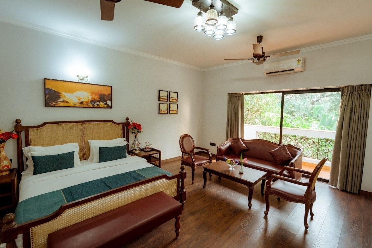 Habitación de hotel con cama, sofá, banca, mesa de centro, ventilador de techo, aire acondicionado y ventana con vistas.