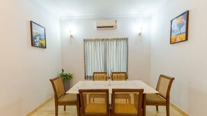 A dining area with a marble table, wicker chairs, a potted plant, and a window with curtains. - Reebah Inn & Suites (Vagator)