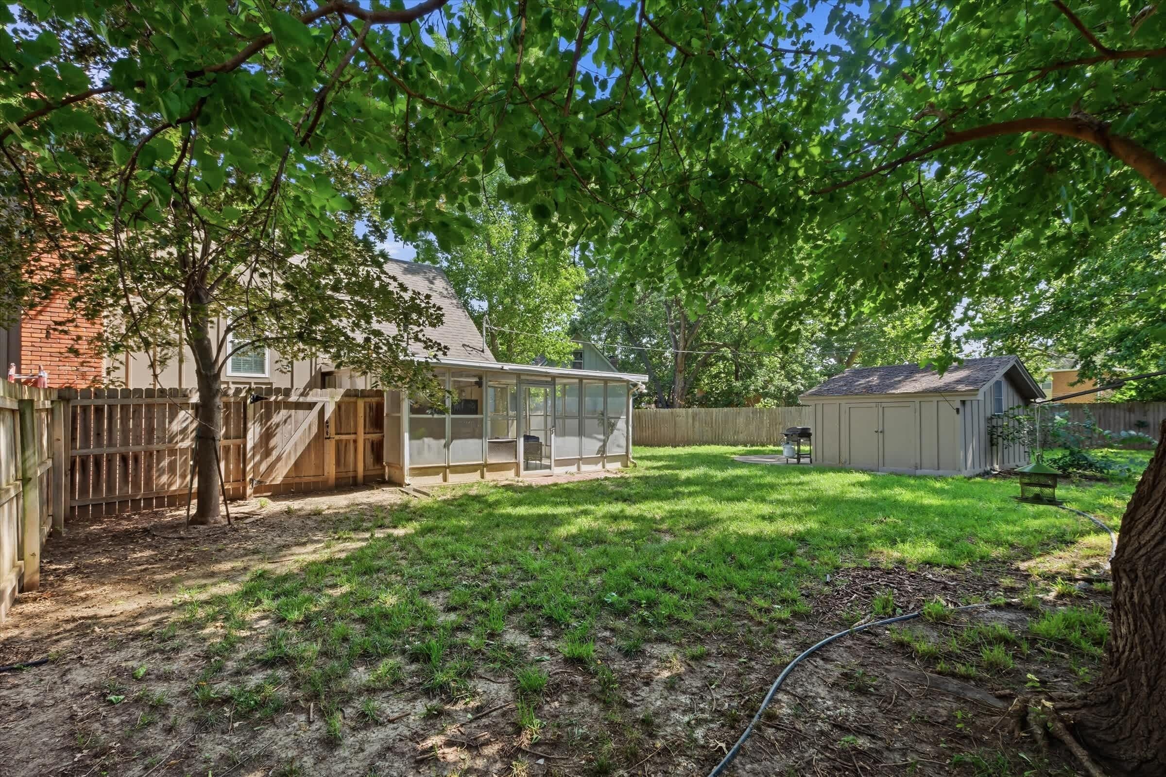 A backyard with a covered patio, a fenced play area, and a shed.