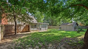 A backyard with a covered patio, a fenced play area, and a shed.