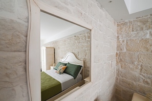 Ein Schlafzimmer mit einer Steinsandsteinwand, einem Bett mit weißem Kopfteil und einem Spiegel, der den Raum reflektiert.